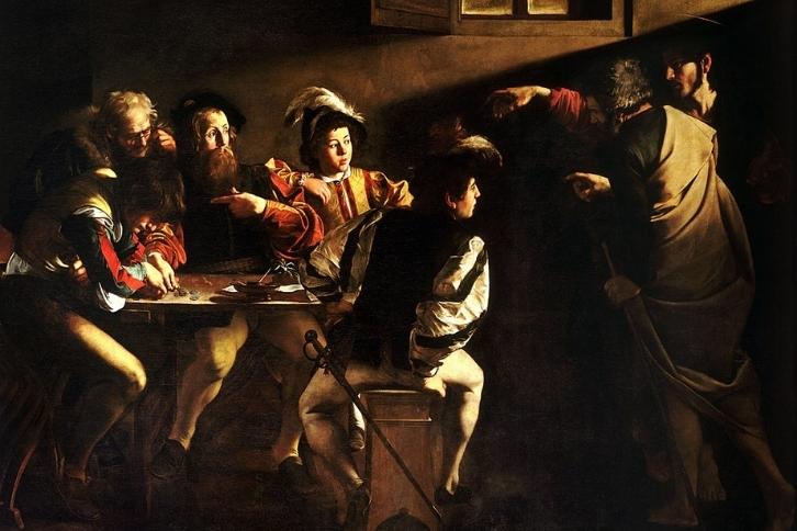 Several men sit around a table, looking to the right and one who is pointing back at them